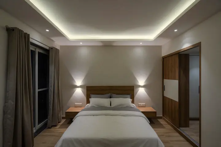 Bedroom at night with a glowing ceiling cove strip, small COB downlights and two up-down wall lights beside the bed