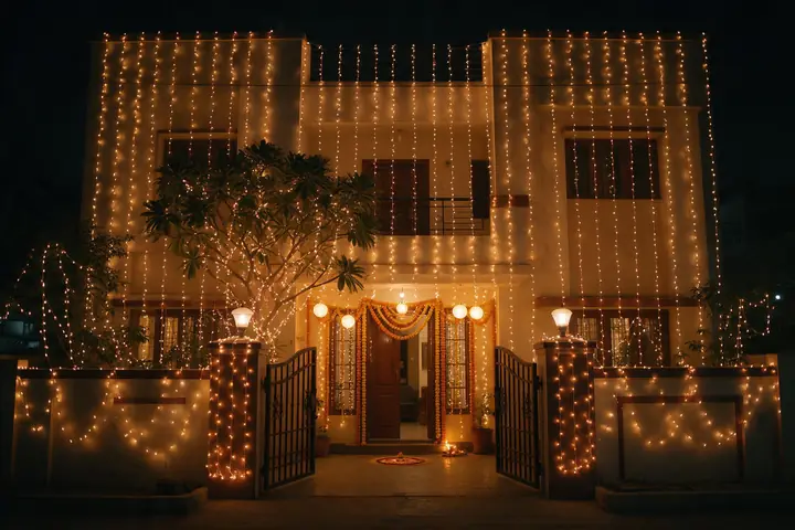 House front decorated for a wedding at night with curtains of warm white string lights, lit trees and marigold garlands