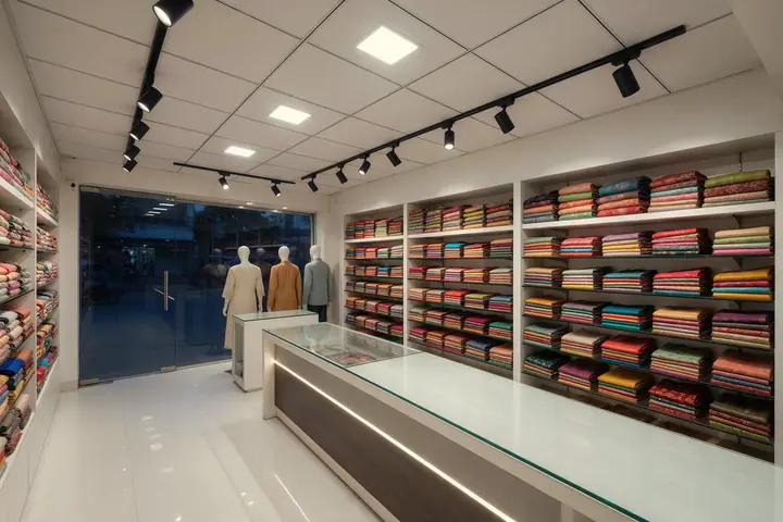 Small retail showroom with square LED panel lights in a grid ceiling and black track spotlights aimed at shelves of fabric